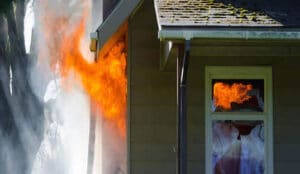 A house engulfed in flames with fire billowing out of one of its windows.