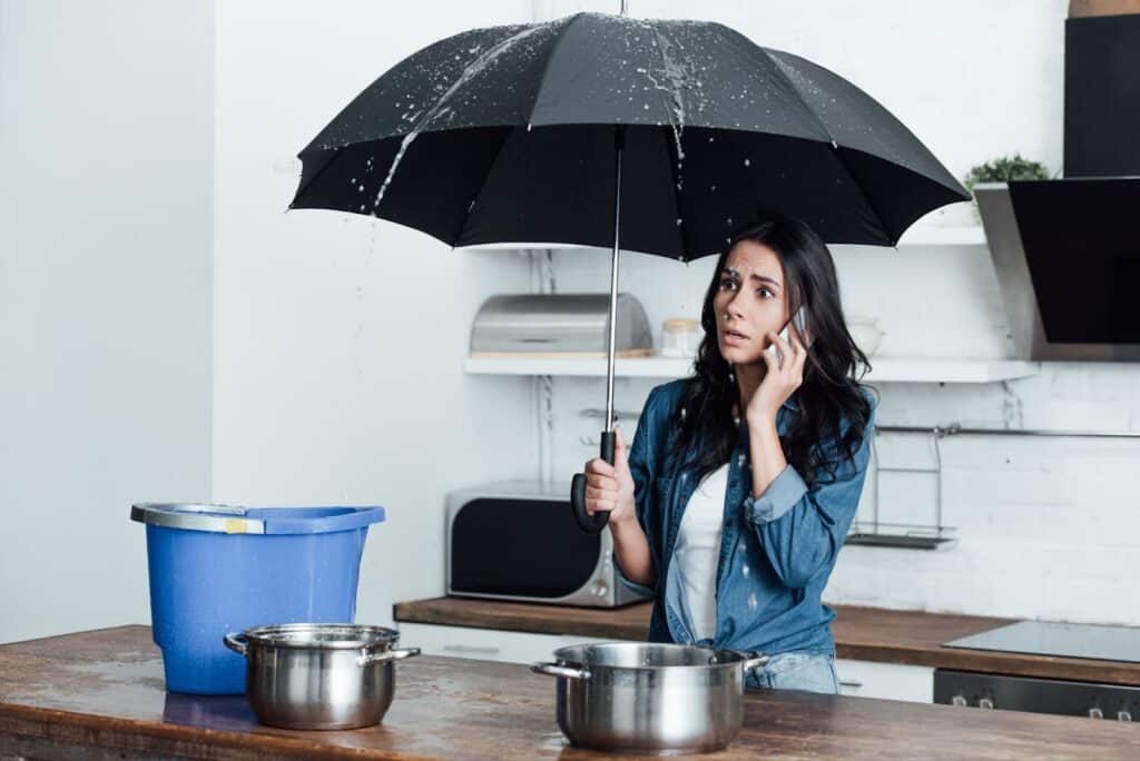 Woman examining kitchen for water damage while holding umbrella