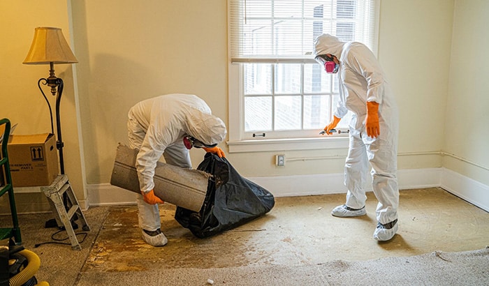 Two men in protective clothing and masks conducting water damage restoration and repair in a room.